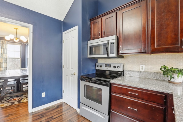 kitchen featuring appliances with stainless steel finishes, dark hardwood / wood-style flooring, light stone countertops, and decorative backsplash