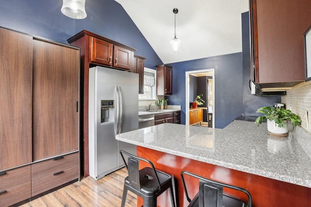 kitchen with a breakfast bar, vaulted ceiling, pendant lighting, stainless steel appliances, and light stone countertops