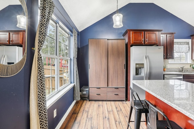 kitchen featuring lofted ceiling, light stone counters, hardwood / wood-style flooring, pendant lighting, and stainless steel appliances