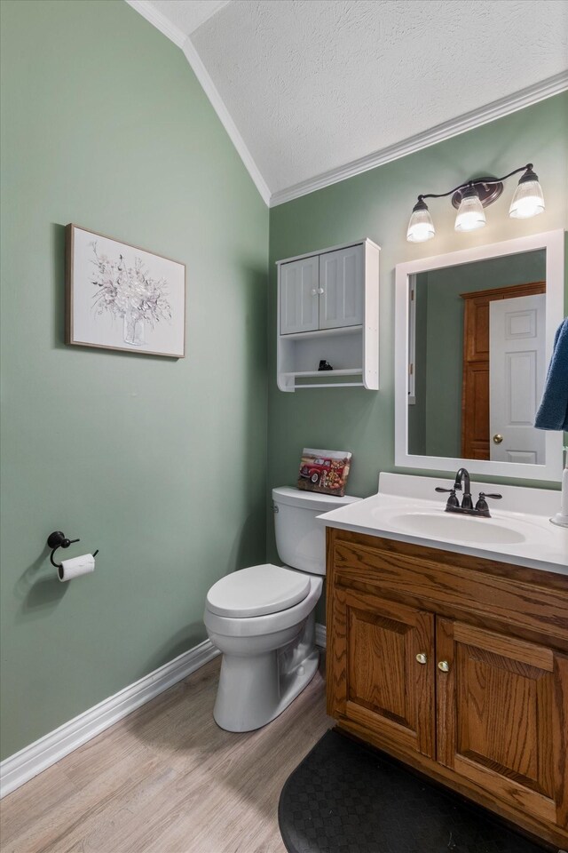 bathroom with lofted ceiling, vanity, wood-type flooring, ornamental molding, and toilet