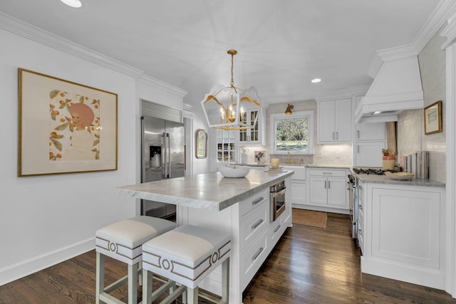 kitchen with hanging light fixtures, high end appliances, white cabinets, a kitchen island, and custom exhaust hood