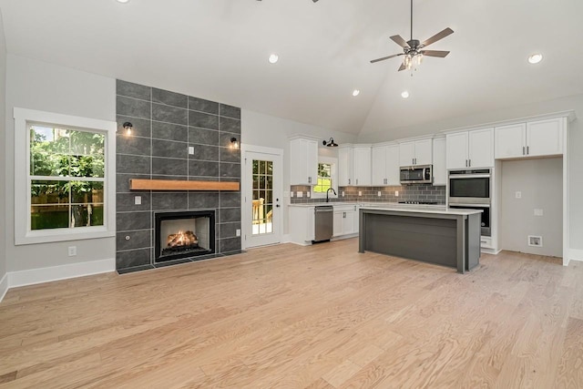 kitchen featuring a tile fireplace, open floor plan, stainless steel appliances, light countertops, and white cabinetry