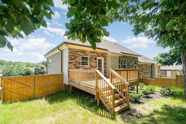 back of house featuring stone siding, roof with shingles, fence, and a wooden deck