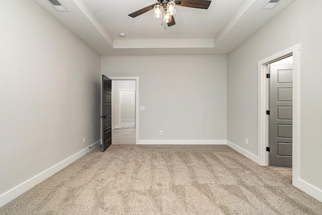 unfurnished room featuring a tray ceiling, carpet, visible vents, and baseboards