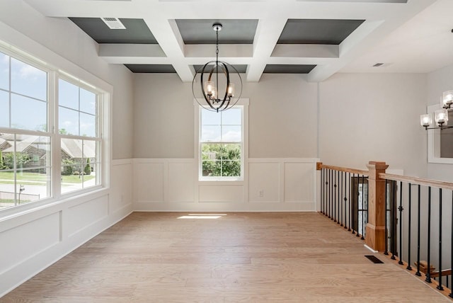 empty room with light wood finished floors, plenty of natural light, beam ceiling, and an inviting chandelier