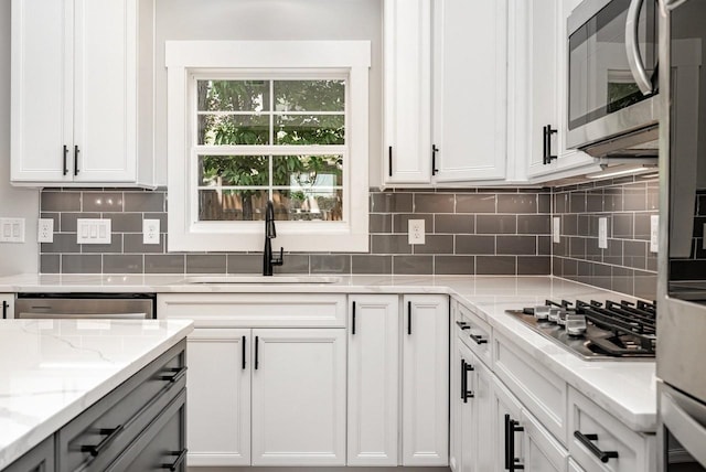 kitchen with light stone countertops, stainless steel appliances, a sink, white cabinetry, and decorative backsplash