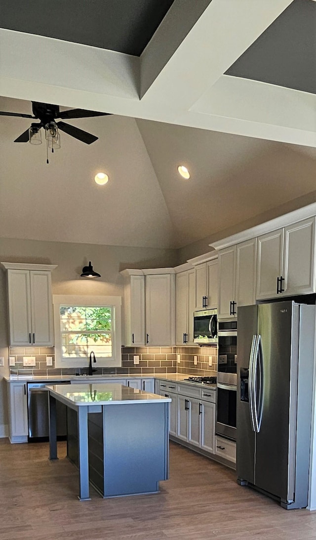 kitchen featuring decorative backsplash, white cabinets, lofted ceiling, a kitchen island, and appliances with stainless steel finishes