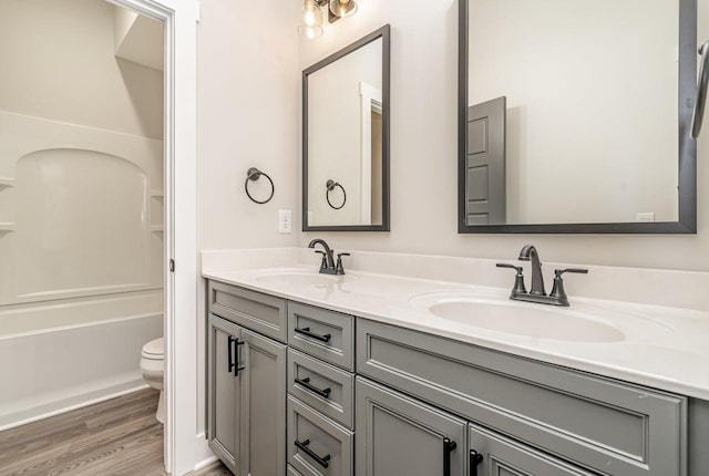 bathroom featuring toilet, double vanity, a sink, and wood finished floors