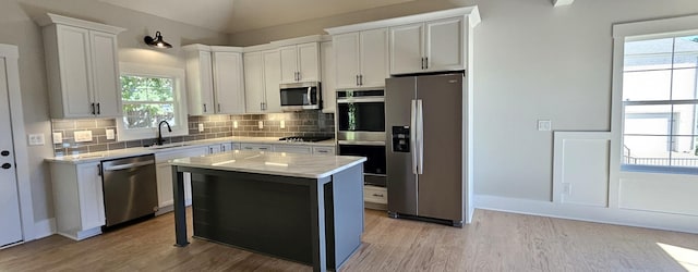 kitchen with appliances with stainless steel finishes, a sink, light wood-style flooring, and decorative backsplash