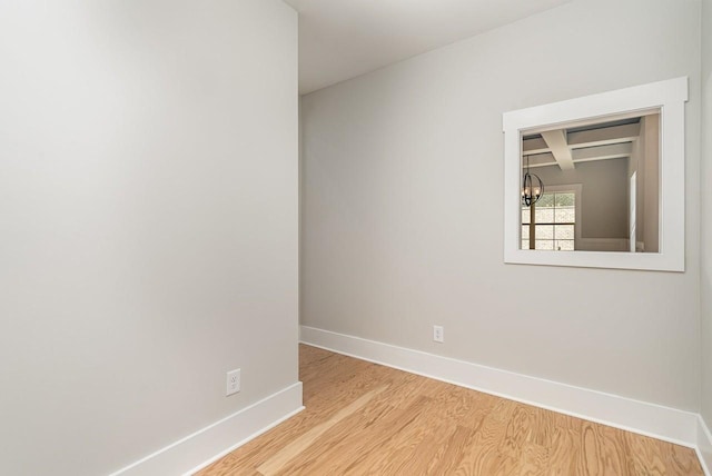 spare room featuring beam ceiling, a notable chandelier, baseboards, and wood finished floors