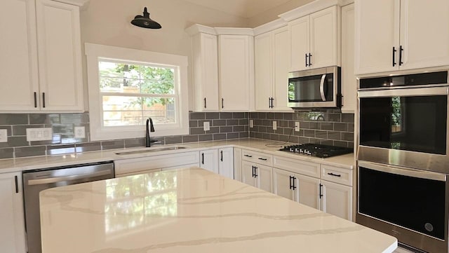 kitchen featuring appliances with stainless steel finishes, a sink, light stone countertops, white cabinetry, and backsplash