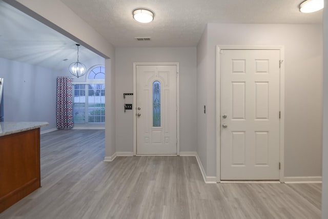 foyer entrance featuring a notable chandelier, light hardwood / wood-style flooring, and a textured ceiling