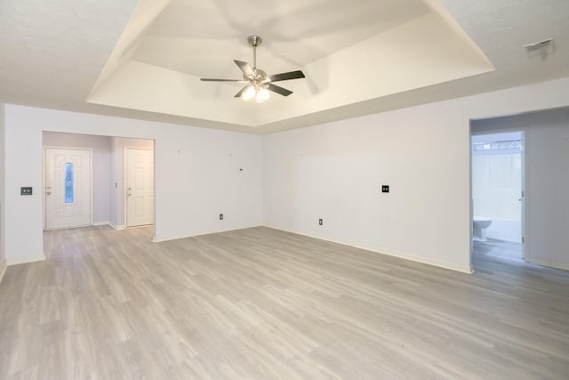 unfurnished room with ceiling fan, light hardwood / wood-style floors, and a tray ceiling