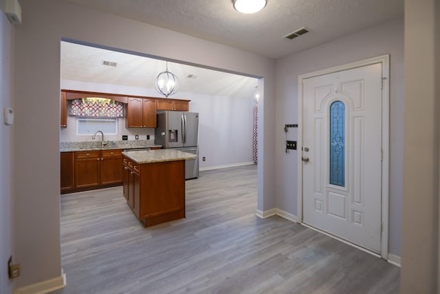 kitchen with sink, wood-type flooring, stainless steel fridge with ice dispenser, a kitchen island, and pendant lighting