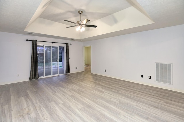 unfurnished room featuring ceiling fan, a raised ceiling, and light hardwood / wood-style flooring