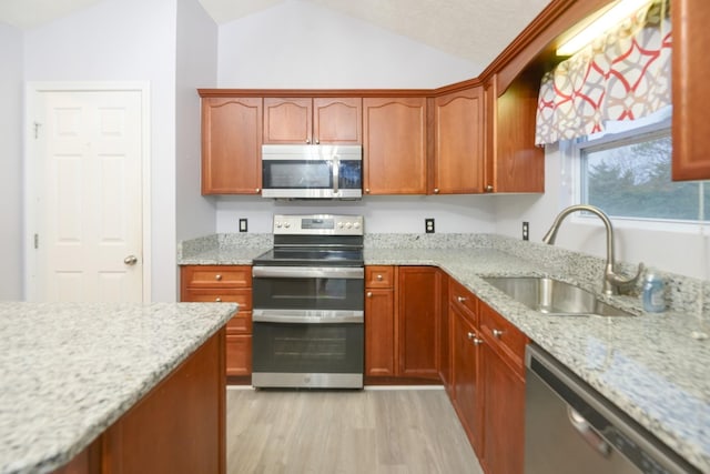 kitchen with light stone counters, appliances with stainless steel finishes, vaulted ceiling, and sink