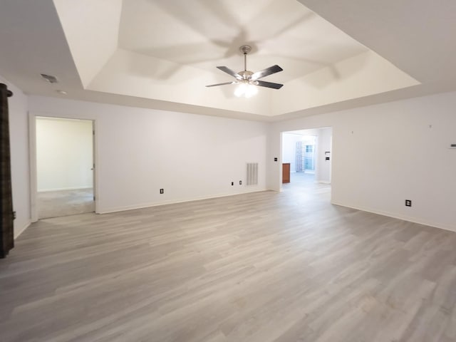 interior space with light hardwood / wood-style flooring, a raised ceiling, and ceiling fan