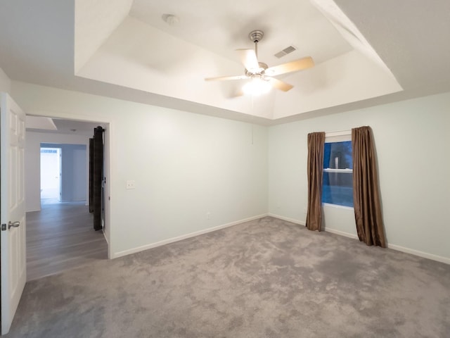 empty room with a raised ceiling, ceiling fan, and carpet flooring