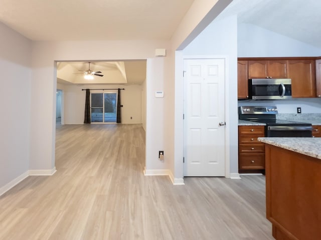 kitchen featuring appliances with stainless steel finishes, a tray ceiling, ceiling fan, light hardwood / wood-style floors, and light stone countertops