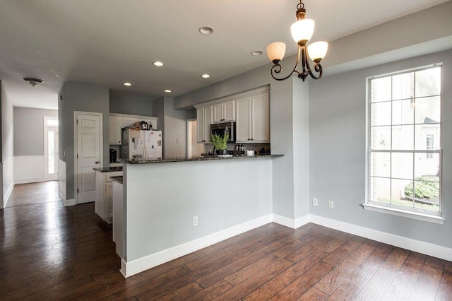 kitchen featuring dark wood-type flooring, dark stone countertops, white refrigerator with ice dispenser, decorative light fixtures, and kitchen peninsula