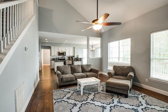 living room with high vaulted ceiling, plenty of natural light, dark hardwood / wood-style flooring, and ceiling fan with notable chandelier