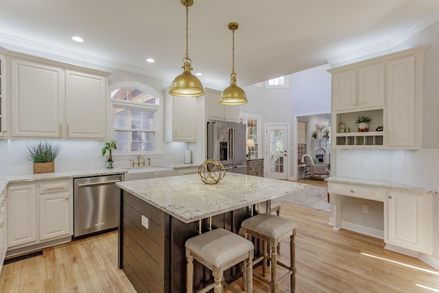 kitchen featuring a kitchen island, appliances with stainless steel finishes, pendant lighting, a kitchen breakfast bar, and light stone counters