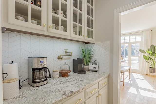 bar with cream cabinetry, light stone countertops, light hardwood / wood-style floors, and backsplash