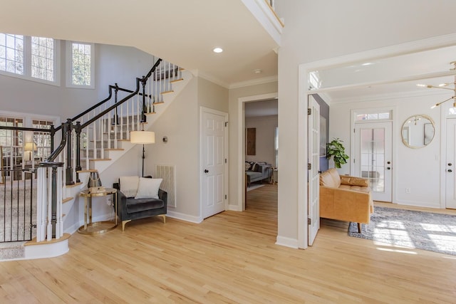 foyer entrance with crown molding, a towering ceiling, light hardwood / wood-style floors, and a wealth of natural light