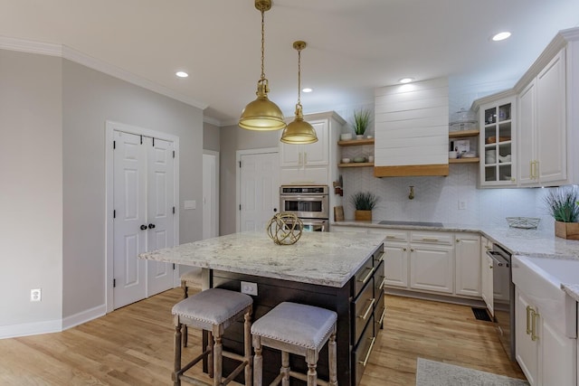 kitchen with white cabinetry, light stone counters, decorative light fixtures, a center island, and ornamental molding