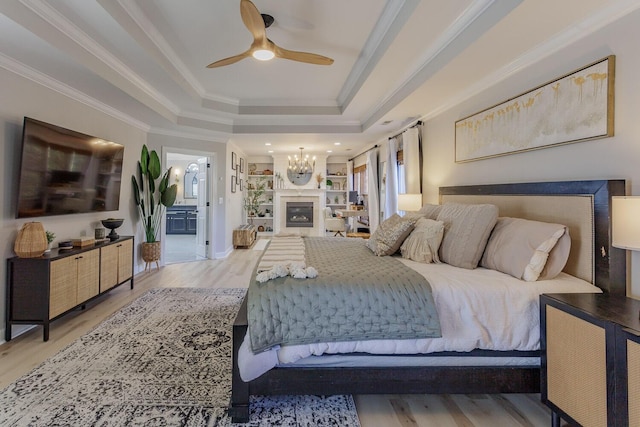 bedroom with ceiling fan with notable chandelier, ornamental molding, light hardwood / wood-style floors, a tray ceiling, and ensuite bath