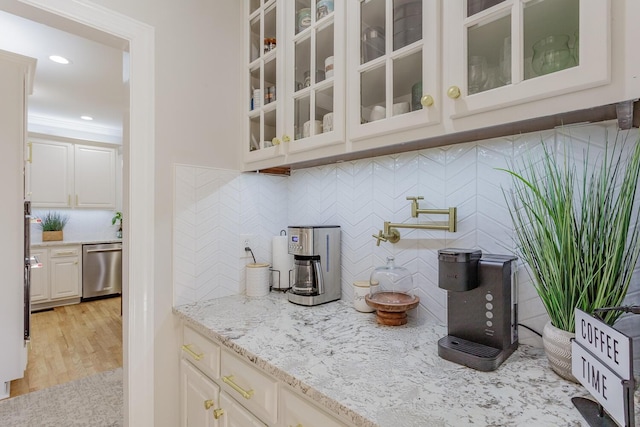 bar featuring backsplash, light stone counters, light hardwood / wood-style floors, white cabinets, and stainless steel dishwasher