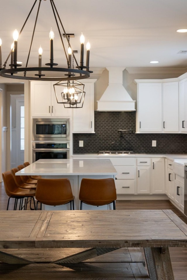 kitchen with dark wood finished floors, custom range hood, appliances with stainless steel finishes, white cabinetry, and backsplash