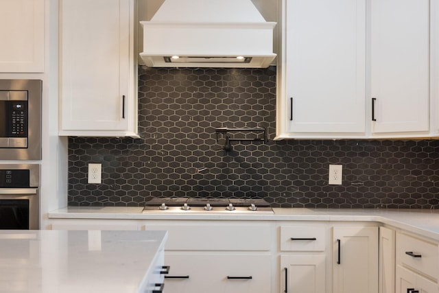 kitchen with stainless steel appliances, premium range hood, white cabinets, and tasteful backsplash