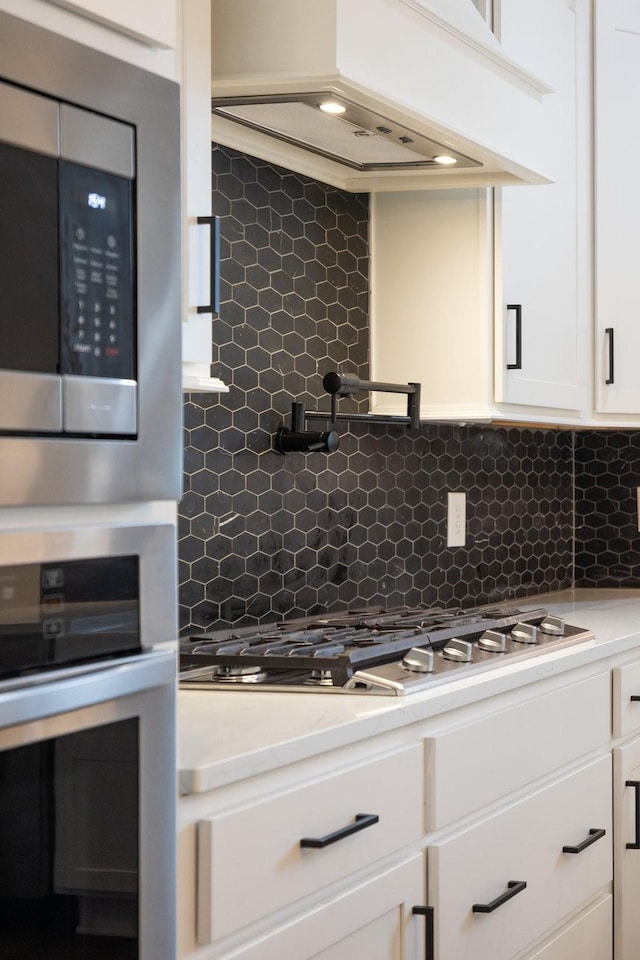 kitchen featuring custom exhaust hood, white cabinetry, appliances with stainless steel finishes, and decorative backsplash