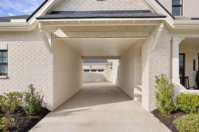 entrance to property with concrete driveway, a shingled roof, and brick siding