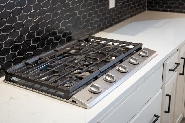 details featuring white cabinetry, stainless steel gas cooktop, decorative backsplash, and light stone countertops