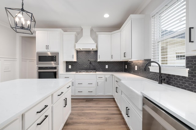 kitchen featuring appliances with stainless steel finishes, wood finished floors, premium range hood, white cabinetry, and a sink