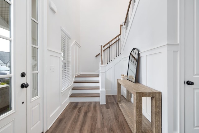 foyer entrance featuring a decorative wall, a high ceiling, stairs, wainscoting, and dark wood-style floors