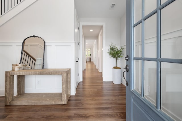 corridor featuring dark wood-type flooring, a wainscoted wall, visible vents, and a decorative wall