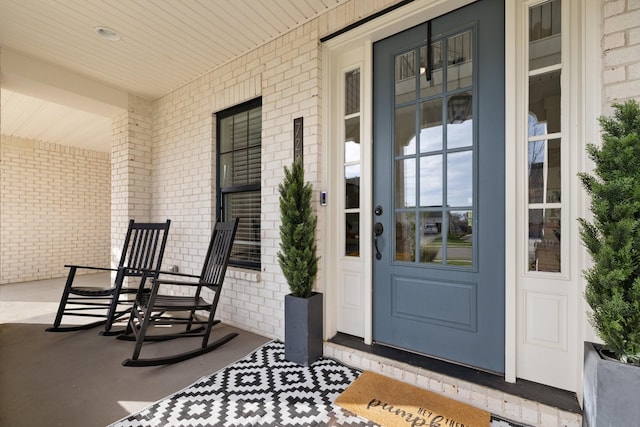 view of exterior entry with a porch and brick siding