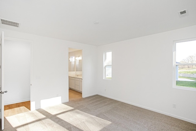 unfurnished bedroom featuring multiple windows, ensuite bathroom, and light colored carpet