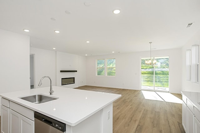 kitchen with sink, white cabinetry, decorative light fixtures, stainless steel dishwasher, and a kitchen island with sink