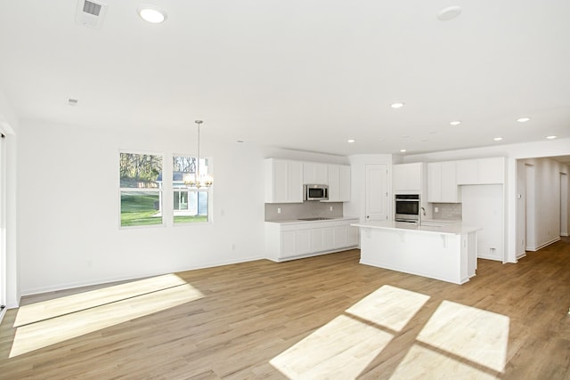 kitchen featuring sink, appliances with stainless steel finishes, tasteful backsplash, white cabinets, and a center island with sink