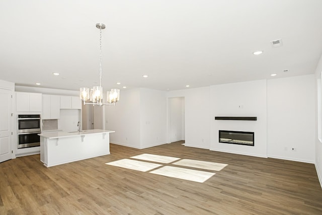 kitchen with a breakfast bar, double oven, decorative light fixtures, white cabinets, and a kitchen island with sink