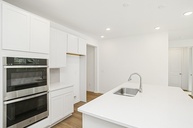 kitchen featuring double oven, white cabinetry, sink, a center island with sink, and light hardwood / wood-style flooring