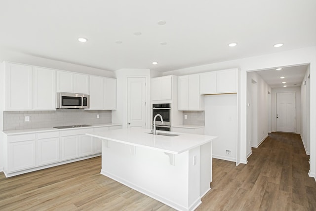 kitchen featuring sink, light wood-type flooring, an island with sink, stainless steel appliances, and white cabinets