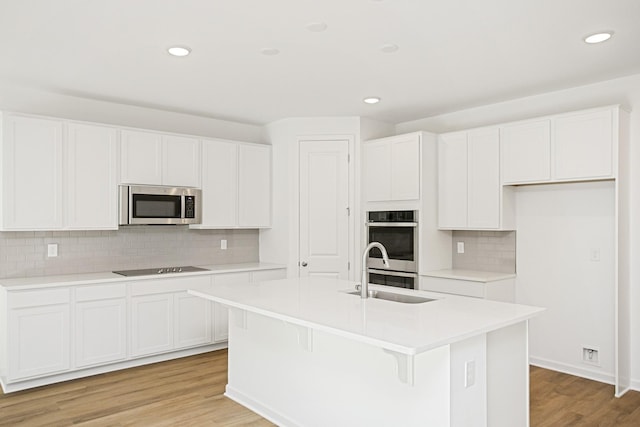 kitchen with an island with sink, appliances with stainless steel finishes, sink, and white cabinets