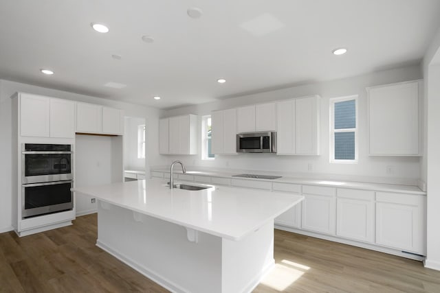 kitchen with sink, white cabinetry, stainless steel appliances, a center island with sink, and light wood-type flooring