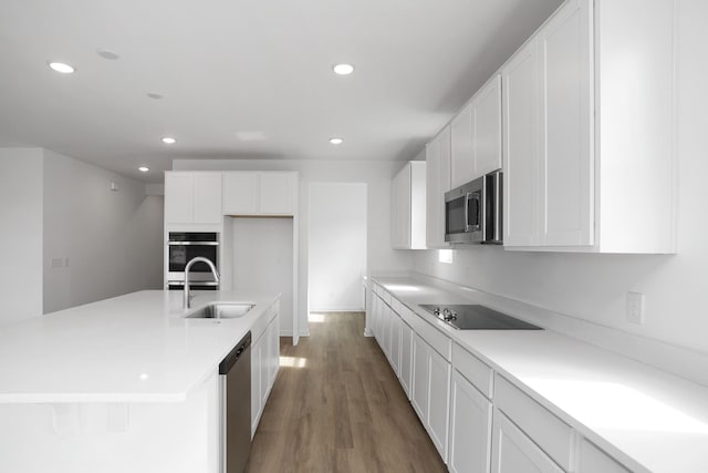 kitchen with sink, white cabinetry, appliances with stainless steel finishes, hardwood / wood-style flooring, and a kitchen island with sink