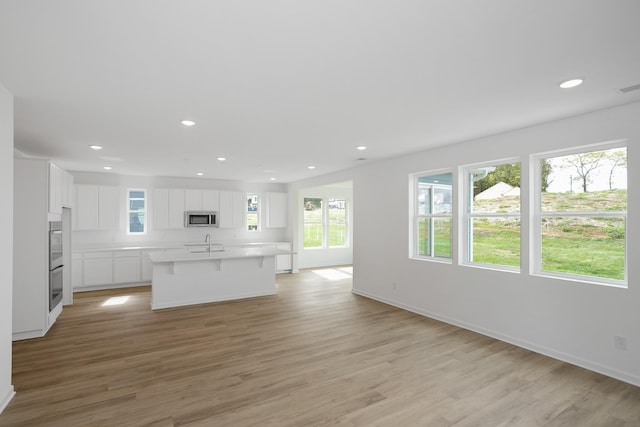 kitchen featuring white cabinetry, sink, a kitchen bar, light hardwood / wood-style floors, and a center island with sink